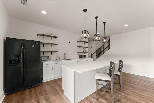 kitchen with open shelves, a sink, white cabinetry, black fridge, and visible vents