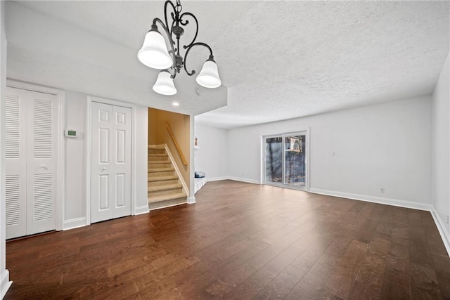 unfurnished living room with dark wood-type flooring, a textured ceiling, and an inviting chandelier