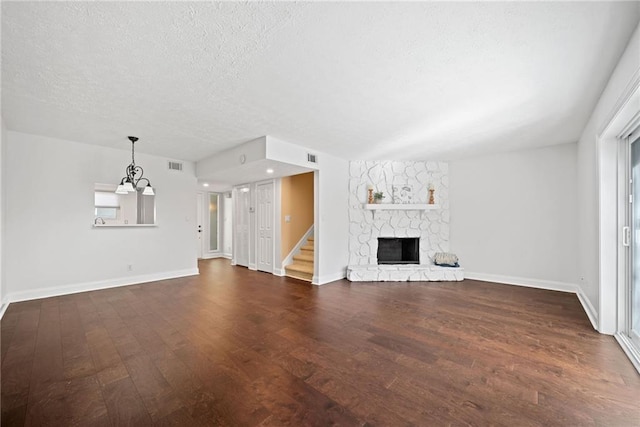 unfurnished living room with a textured ceiling, a notable chandelier, dark hardwood / wood-style flooring, and a fireplace