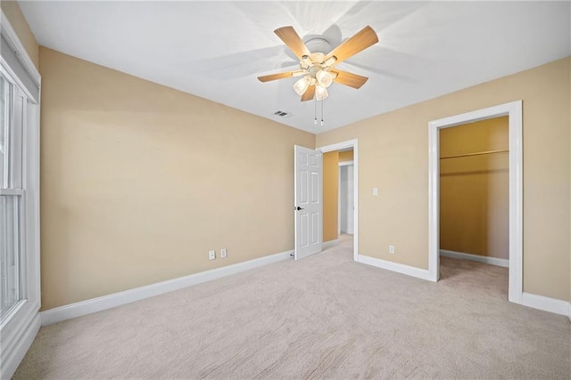 unfurnished bedroom with a walk in closet, ceiling fan, a closet, and light carpet