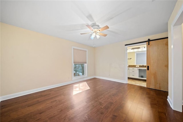 unfurnished bedroom featuring a barn door, ceiling fan, hardwood / wood-style floors, and ensuite bath