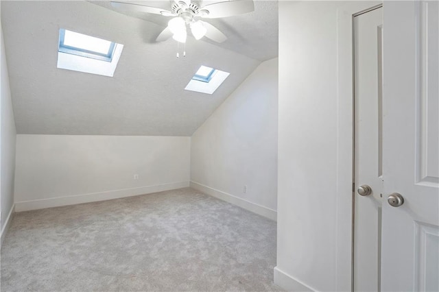 additional living space featuring ceiling fan, light colored carpet, and vaulted ceiling with skylight