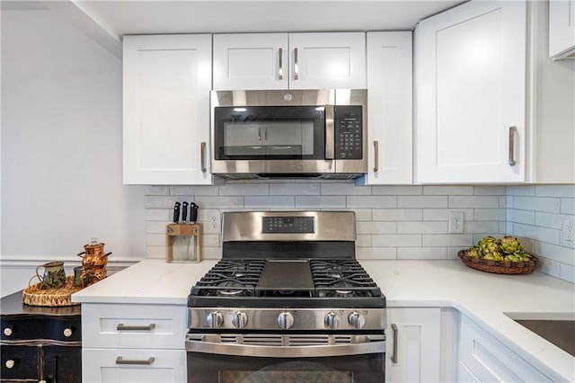 kitchen with white cabinets, backsplash, light stone counters, and appliances with stainless steel finishes