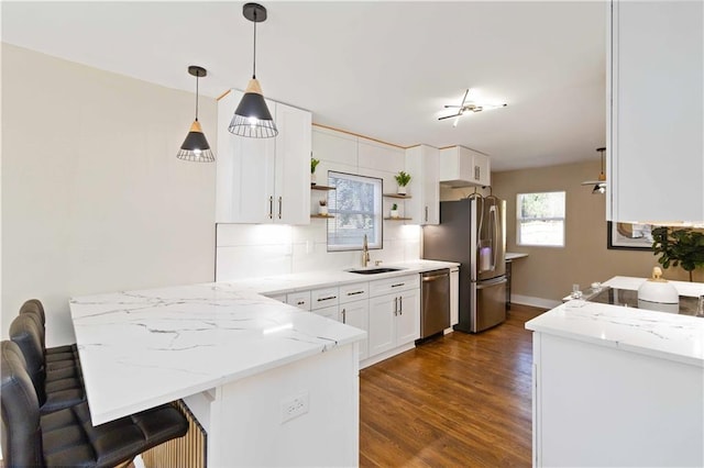 kitchen with sink, appliances with stainless steel finishes, white cabinetry, light stone countertops, and kitchen peninsula