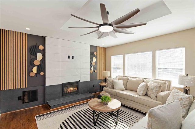 living room featuring a tiled fireplace, wood-type flooring, and ceiling fan