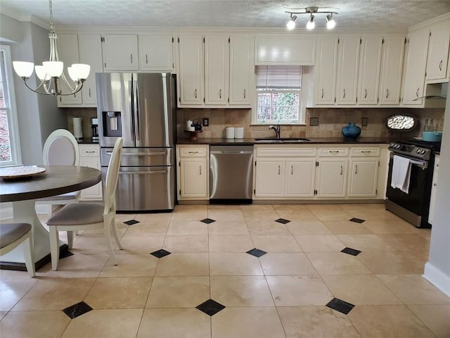 kitchen with stainless steel appliances, dark countertops, backsplash, an inviting chandelier, and a sink