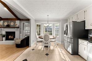 kitchen featuring dishwashing machine, light wood-style flooring, freestanding refrigerator, a fireplace, and white cabinetry