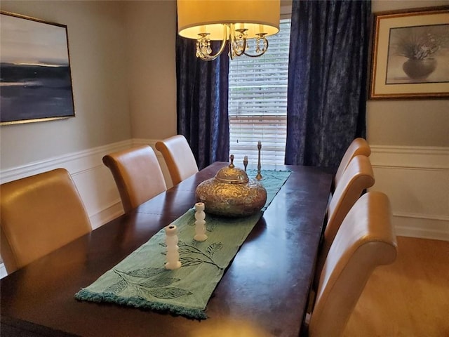 dining space featuring wainscoting, a decorative wall, and an inviting chandelier