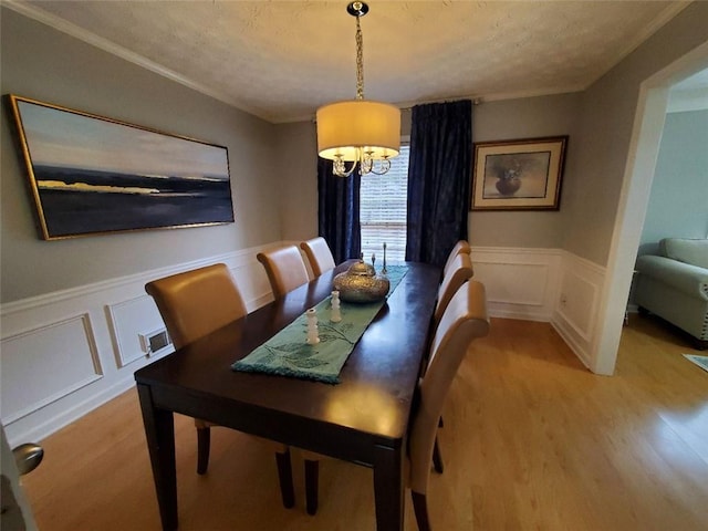 dining space with visible vents, wainscoting, ornamental molding, light wood-type flooring, and a decorative wall