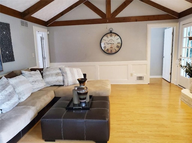 living area featuring wainscoting, visible vents, vaulted ceiling with beams, and wood finished floors