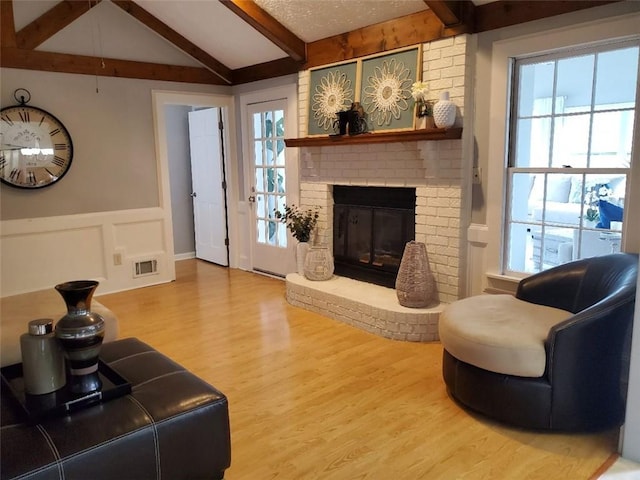 living area with a brick fireplace, visible vents, vaulted ceiling with beams, and wood finished floors