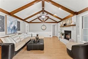 living room featuring a decorative wall, lofted ceiling with beams, a brick fireplace, wainscoting, and wood finished floors