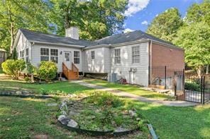 back of property with entry steps, a lawn, a chimney, and fence