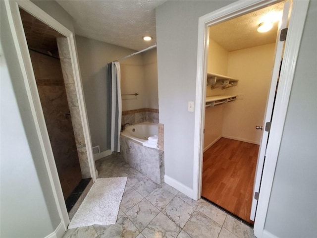 full bath featuring a textured ceiling, a garden tub, baseboards, a walk in closet, and walk in shower