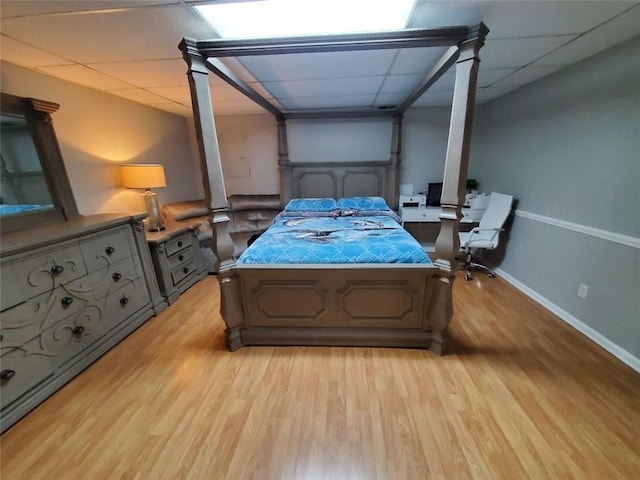 bedroom featuring a paneled ceiling, light wood finished floors, and baseboards