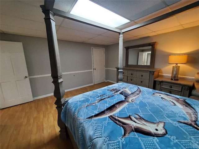 bedroom featuring baseboards, a drop ceiling, and wood finished floors