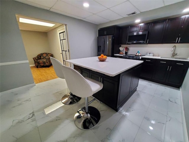 kitchen with visible vents, a kitchen island, marble finish floor, stainless steel appliances, and a sink