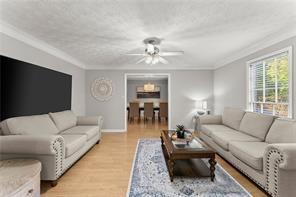 living area with baseboards, a ceiling fan, ornamental molding, a textured ceiling, and light wood-type flooring