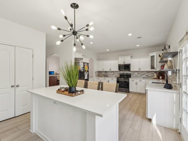 kitchen featuring a sink, a center island, arched walkways, appliances with stainless steel finishes, and decorative backsplash