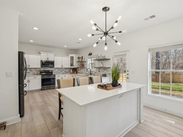 kitchen featuring visible vents, open shelves, stainless steel appliances, decorative backsplash, and a notable chandelier