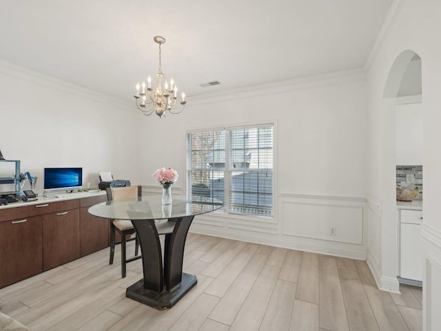 dining area featuring light wood finished floors, visible vents, crown molding, a chandelier, and wainscoting