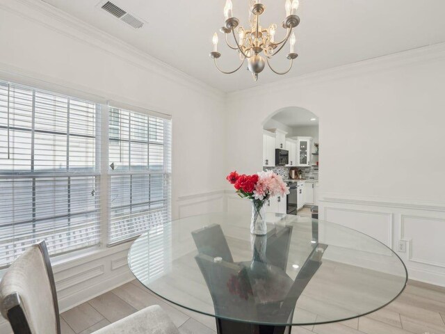 dining room with visible vents, crown molding, a notable chandelier, arched walkways, and a decorative wall