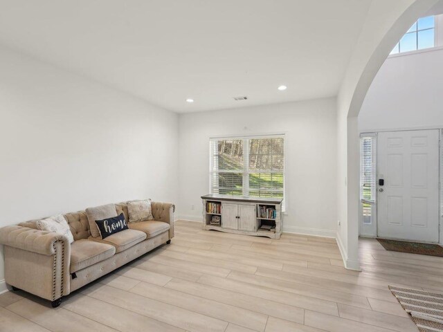 living room featuring baseboards, recessed lighting, arched walkways, and light wood-type flooring
