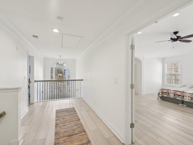 hallway with light wood-style flooring, baseboards, attic access, and ornamental molding