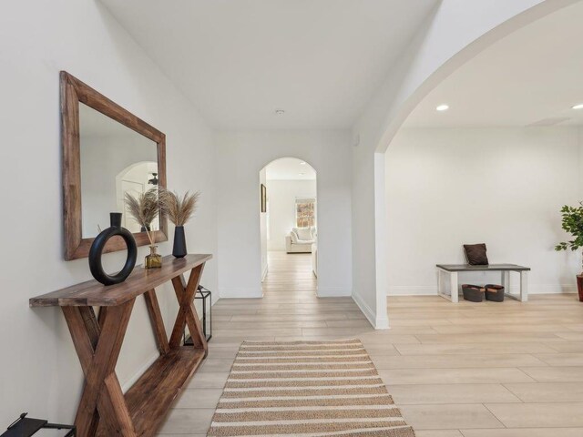 corridor with recessed lighting, light wood-style floors, arched walkways, and baseboards