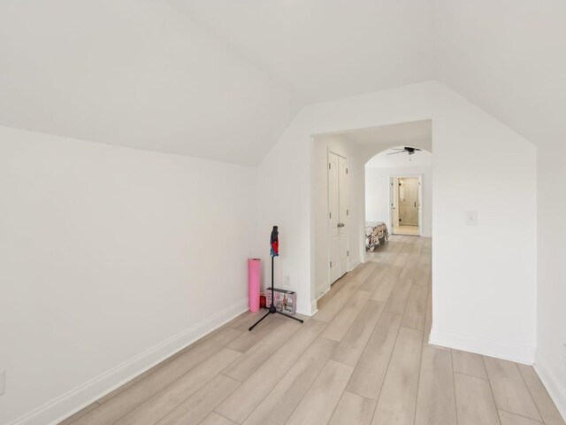 bonus room with light wood finished floors, arched walkways, baseboards, and lofted ceiling