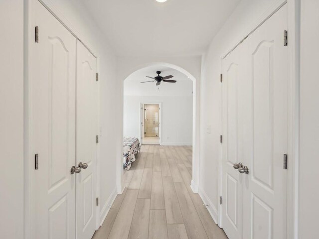 corridor featuring arched walkways, baseboards, and light wood-style floors