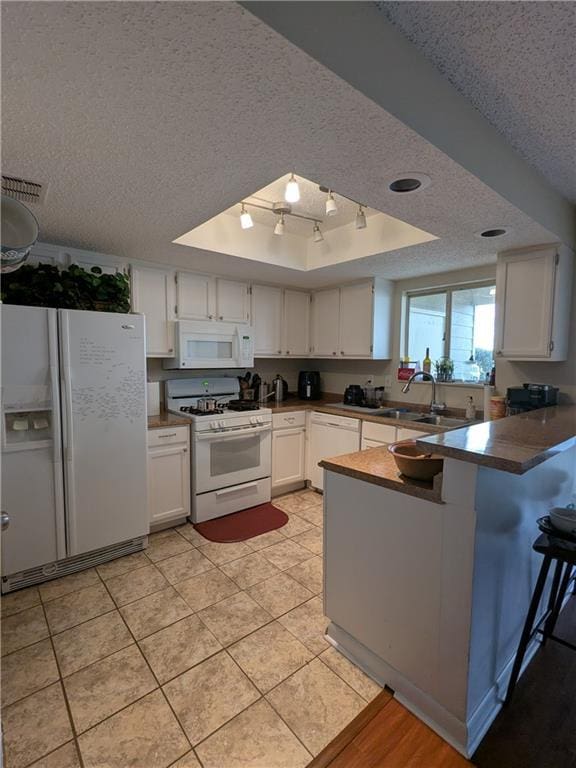 kitchen featuring white appliances, white cabinets, a textured ceiling, kitchen peninsula, and a tray ceiling