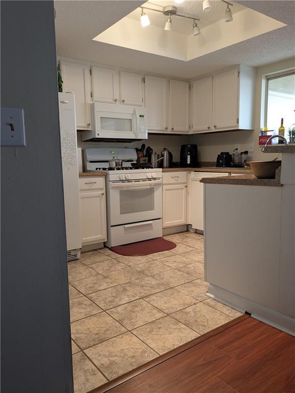 kitchen featuring a tray ceiling, white appliances, white cabinetry, a textured ceiling, and rail lighting