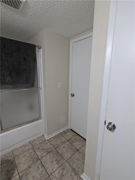 bathroom featuring a textured ceiling, combined bath / shower with glass door, and tile patterned flooring