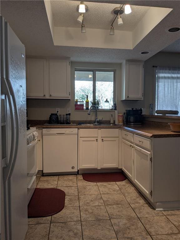 kitchen with a raised ceiling, white appliances, white cabinetry, and rail lighting