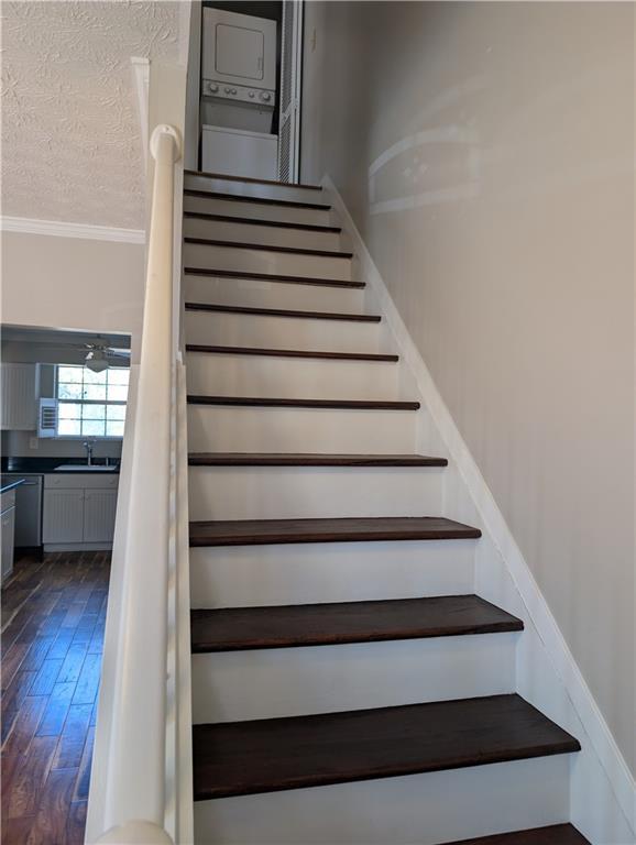 stairway with stacked washer / drying machine, sink, wood-type flooring, a textured ceiling, and ornamental molding