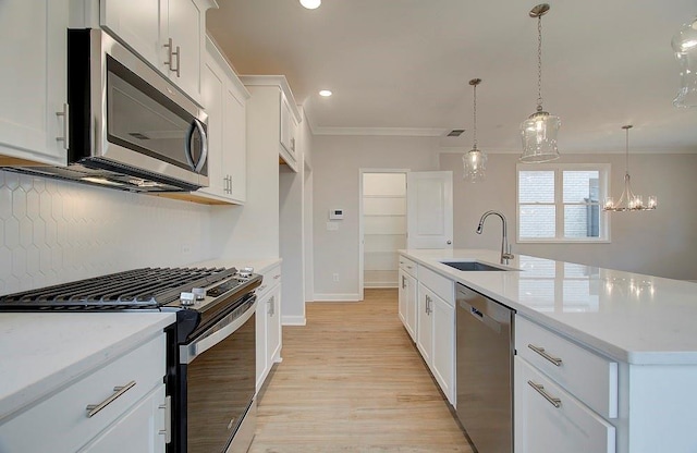 kitchen with pendant lighting, sink, crown molding, appliances with stainless steel finishes, and a center island with sink