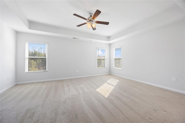 empty room with ceiling fan, light colored carpet, and a tray ceiling