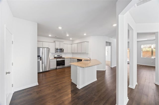 kitchen featuring appliances with stainless steel finishes, white cabinetry, tasteful backsplash, kitchen peninsula, and light stone counters