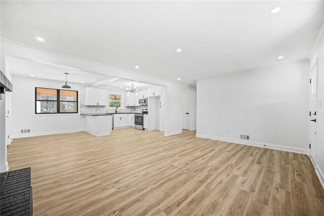 unfurnished living room with light wood finished floors, recessed lighting, baseboards, a sink, and a chandelier