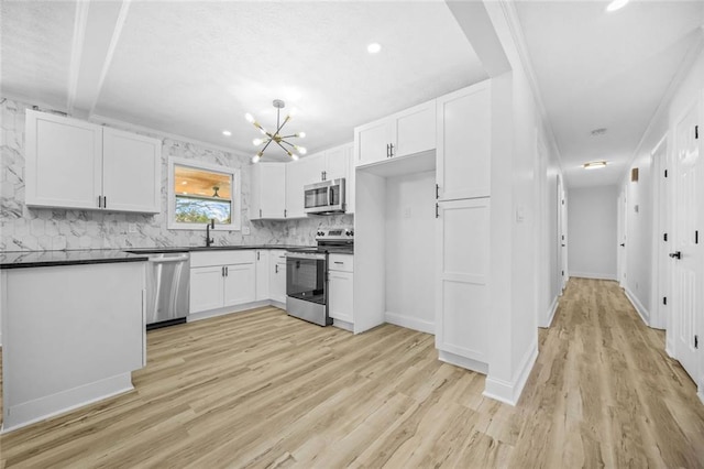 kitchen with appliances with stainless steel finishes, dark countertops, light wood finished floors, a sink, and white cabinets