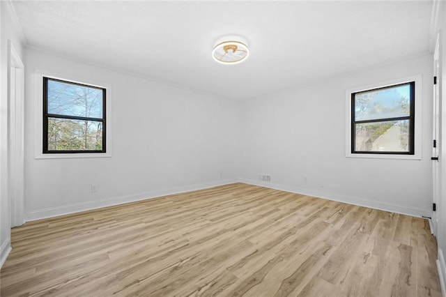 spare room with crown molding, light wood-style floors, and baseboards