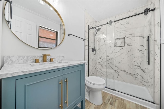 bathroom with a marble finish shower, toilet, wood finished floors, vanity, and ornamental molding