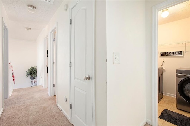 corridor with a textured ceiling, light carpet, and washer / clothes dryer