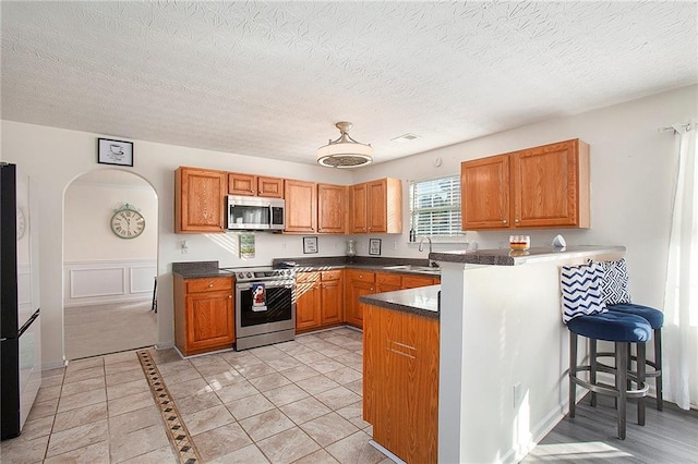 kitchen featuring a kitchen breakfast bar, sink, a textured ceiling, kitchen peninsula, and stainless steel appliances