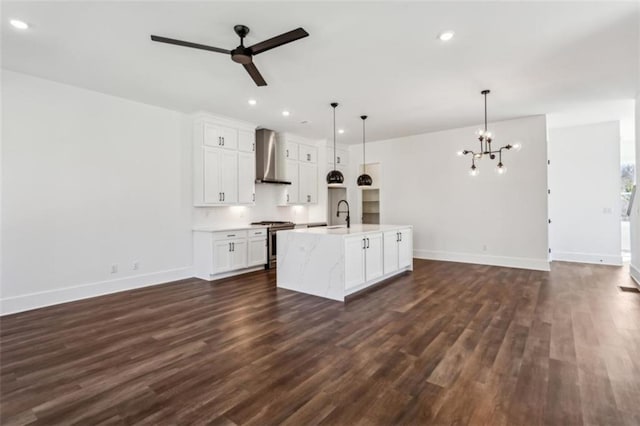 kitchen with wall chimney range hood, open floor plan, ceiling fan with notable chandelier, stainless steel gas range, and dark wood-style flooring