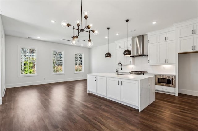 kitchen with an inviting chandelier, a sink, stainless steel appliances, white cabinets, and wall chimney range hood