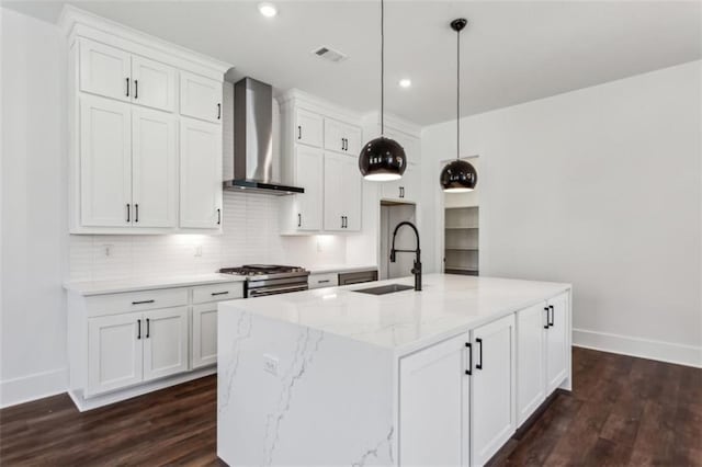 kitchen featuring visible vents, stainless steel gas stove, a sink, white cabinetry, and wall chimney range hood