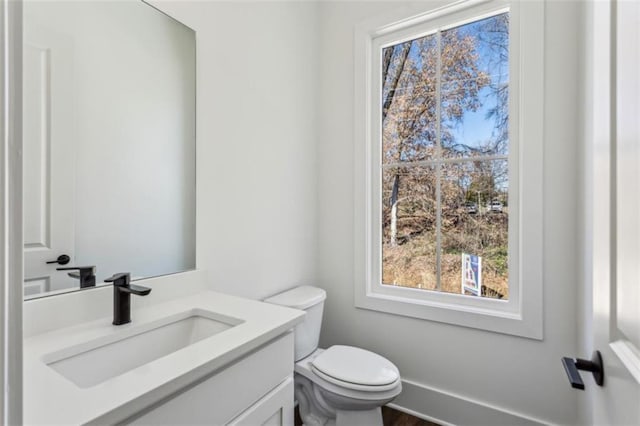 half bath featuring baseboards, toilet, and vanity