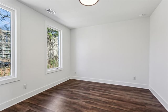 unfurnished room with dark wood-style floors, visible vents, and baseboards